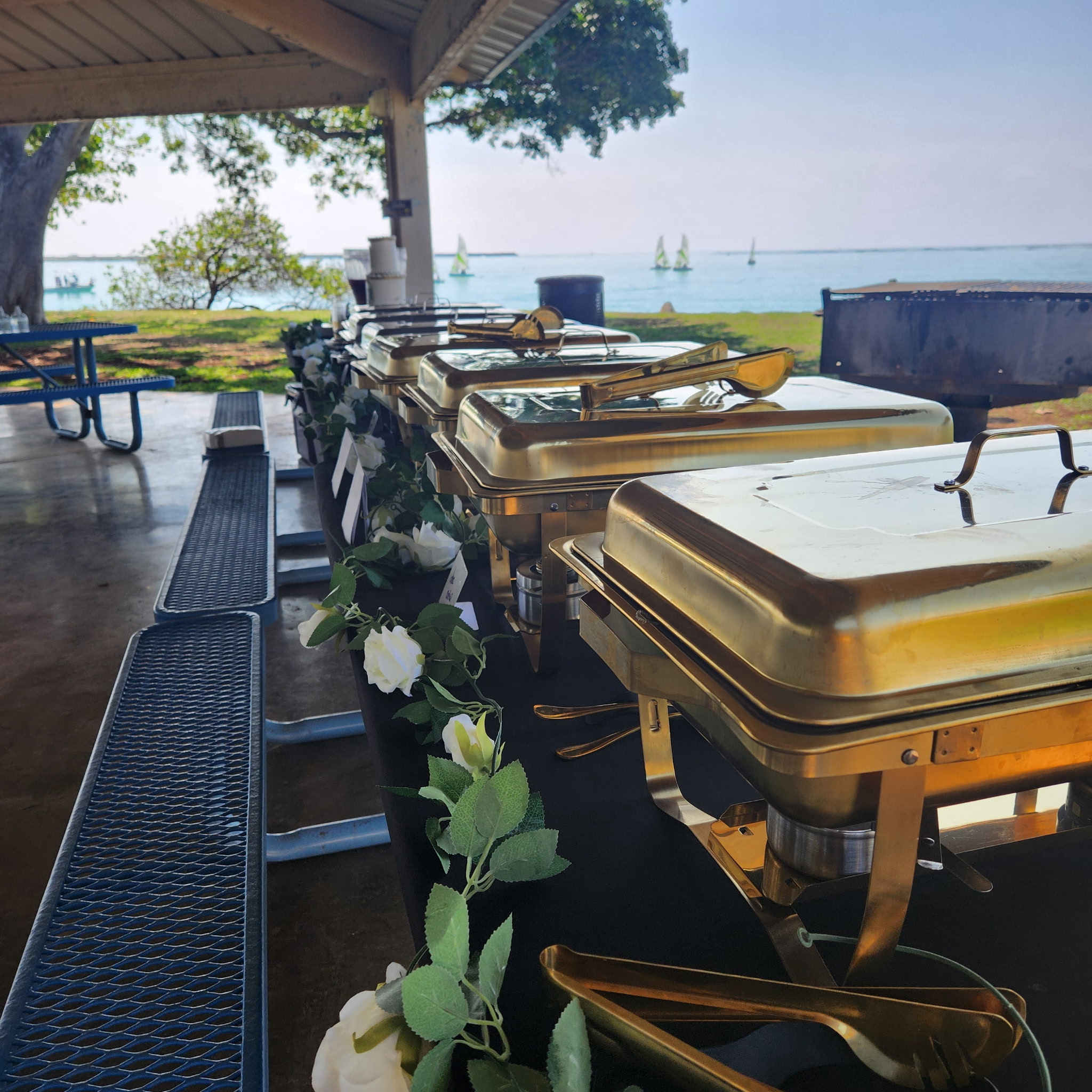 Gold chafing dishes lined up with ocean view and white rose garland
