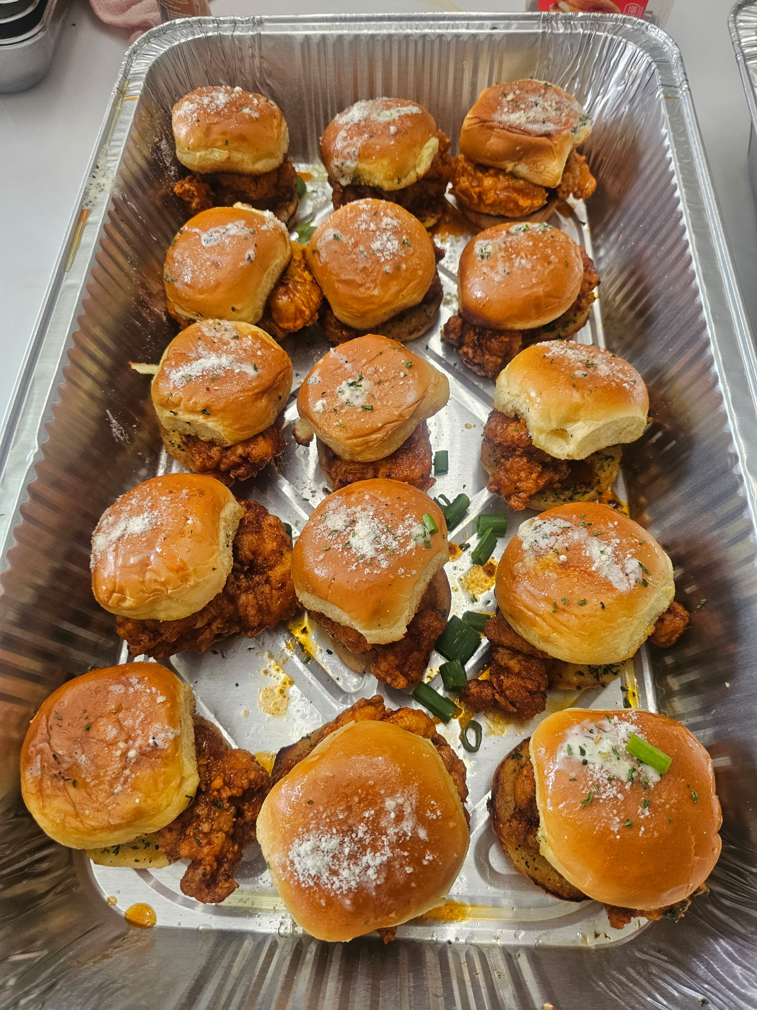 Tray of golden chicken sliders with brioche buns and herbs